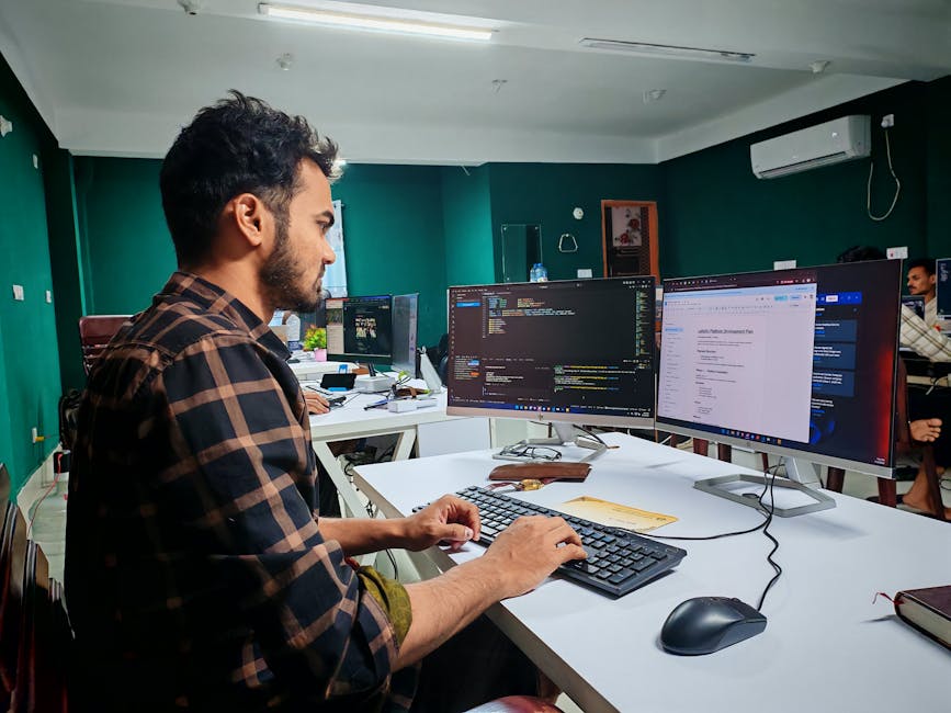 A software developer working on code at a dual monitor setup in a modern office
