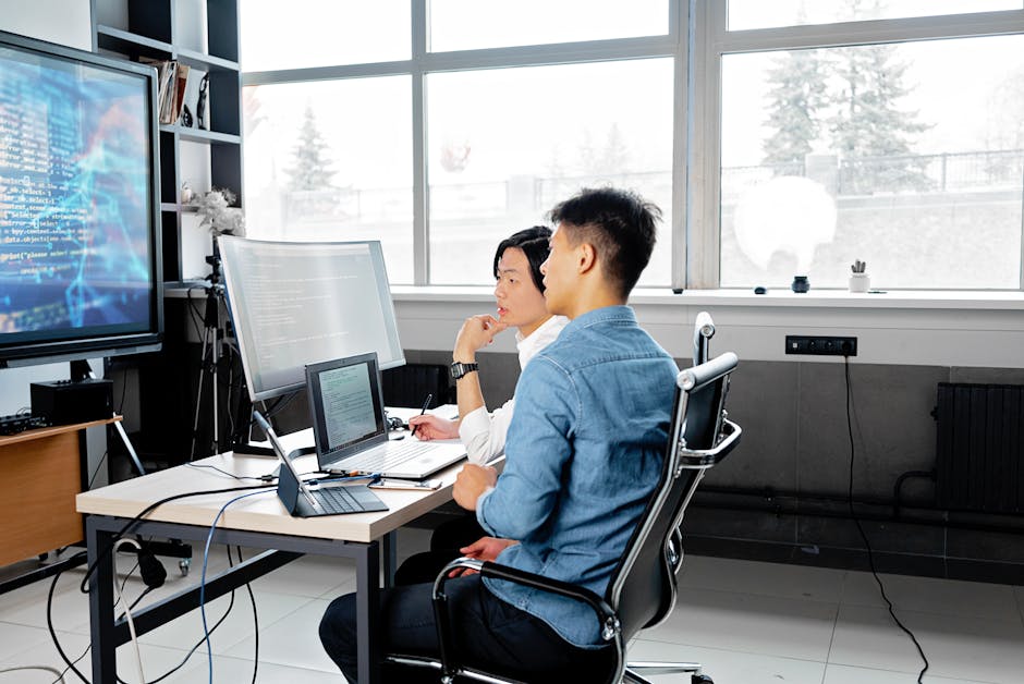 Two men analyzing code on computers in a modern office setting